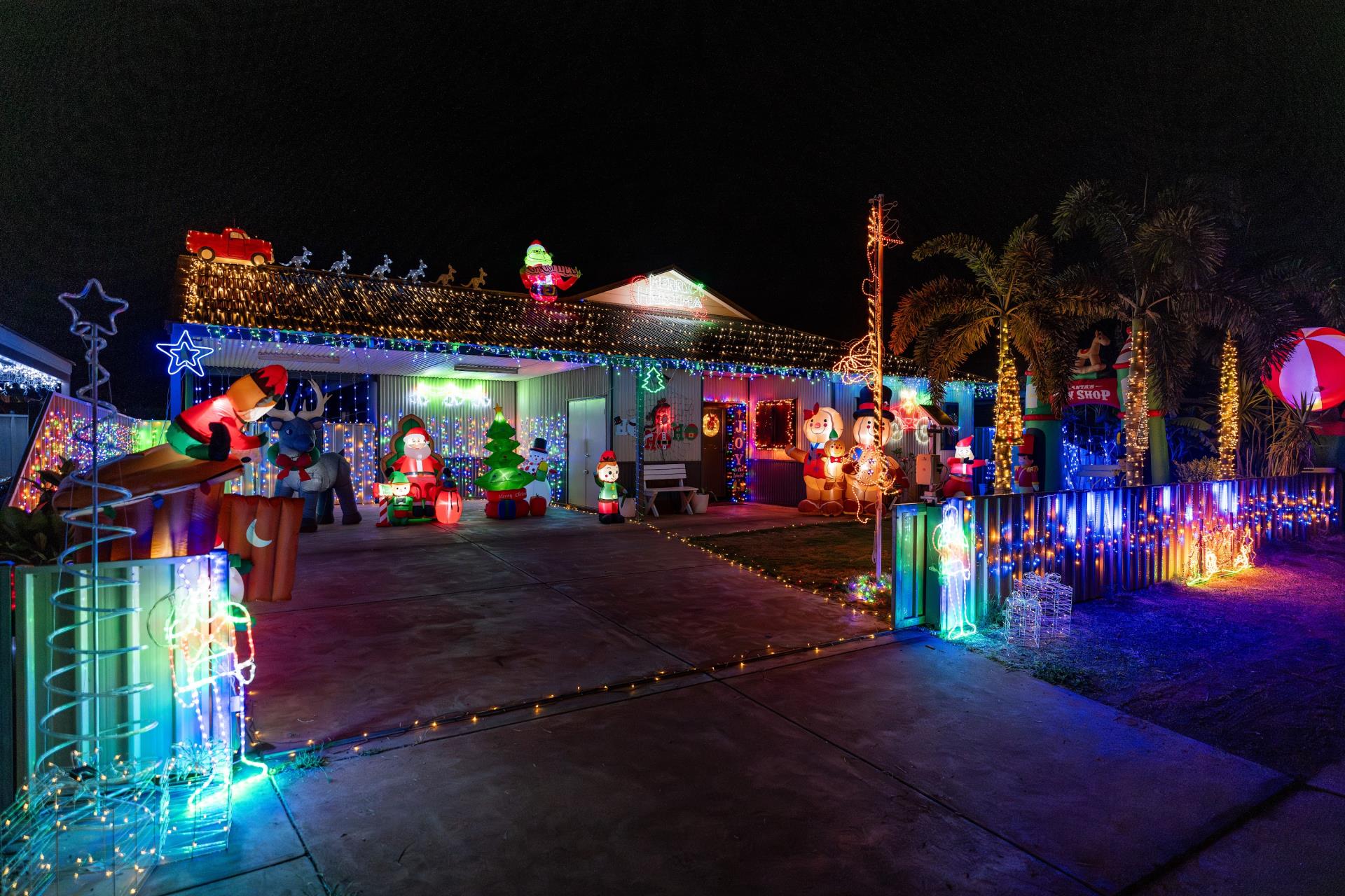 A brightly decorated house for Christmas, featuring colorful lights, inflatable characters, and festive ornaments in a nighttime setting.