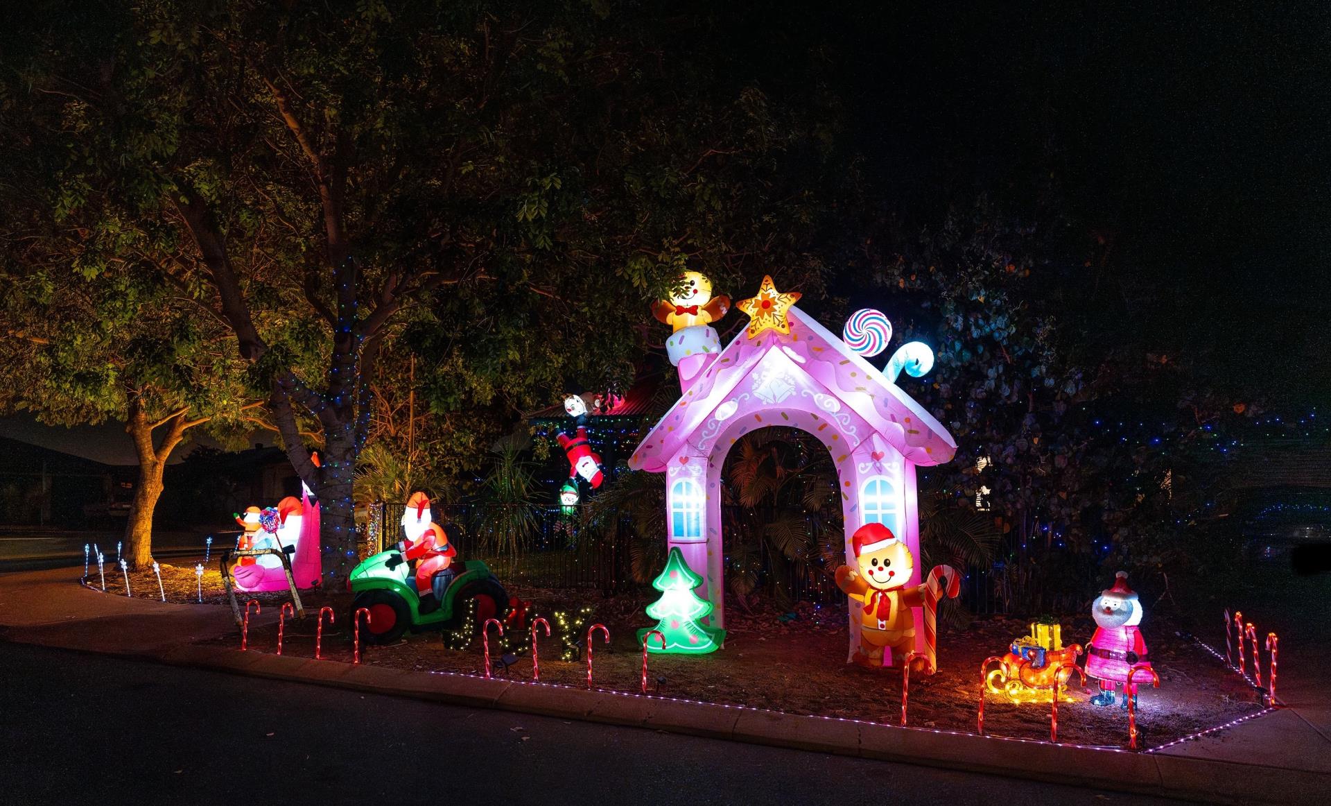 A colorful Christmas display featuring inflatable characters, a candy-themed house, and festive lights in a nighttime setting.