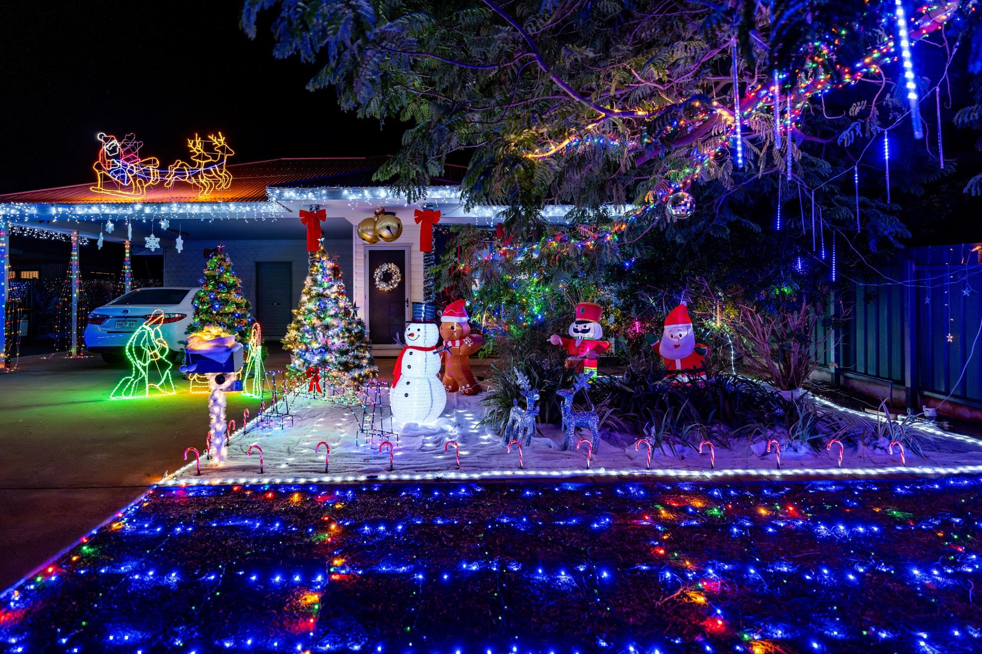 A festive yard decorated with colorful Christmas lights, inflatable characters, and a Christmas tree, all set at night.